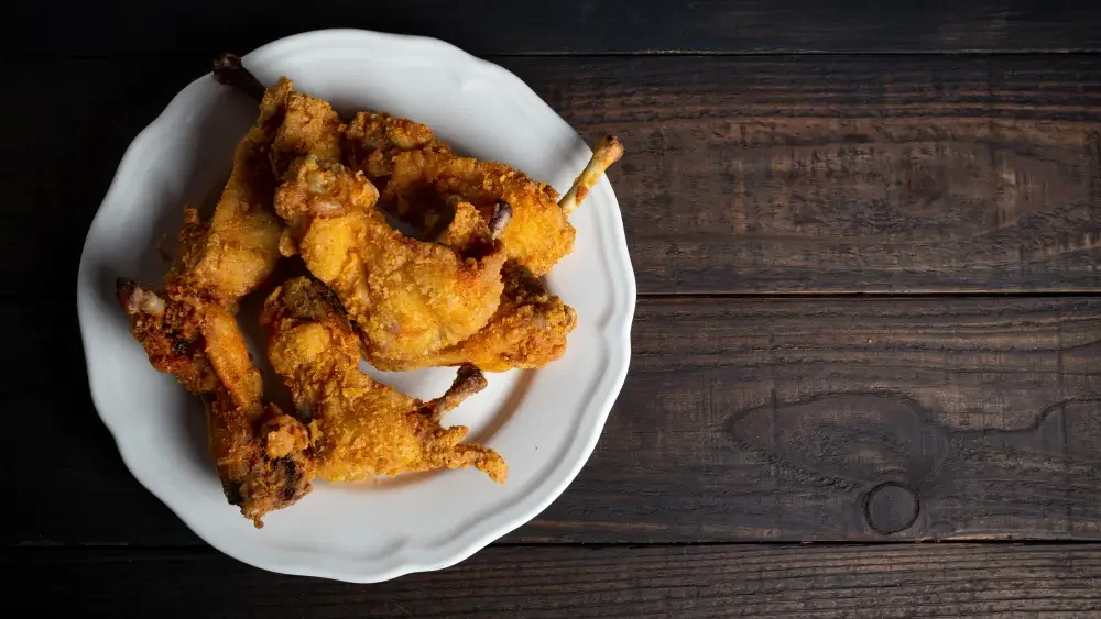 A plate of golden-brown crispy fried chicken served on a white dish, placed on a dark wooden table.