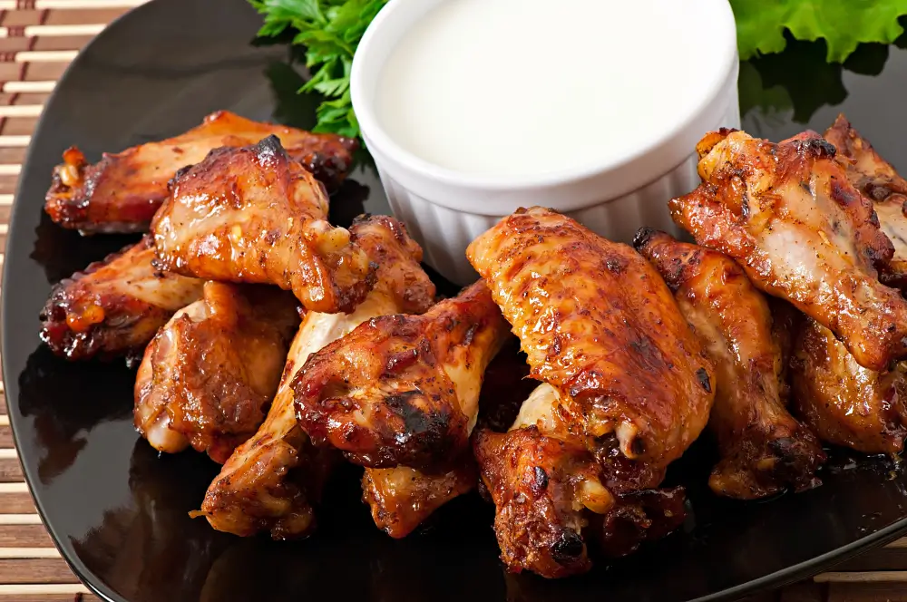 A plate of crispy, glazed boneless chicken wings served with a side of creamy dipping sauce