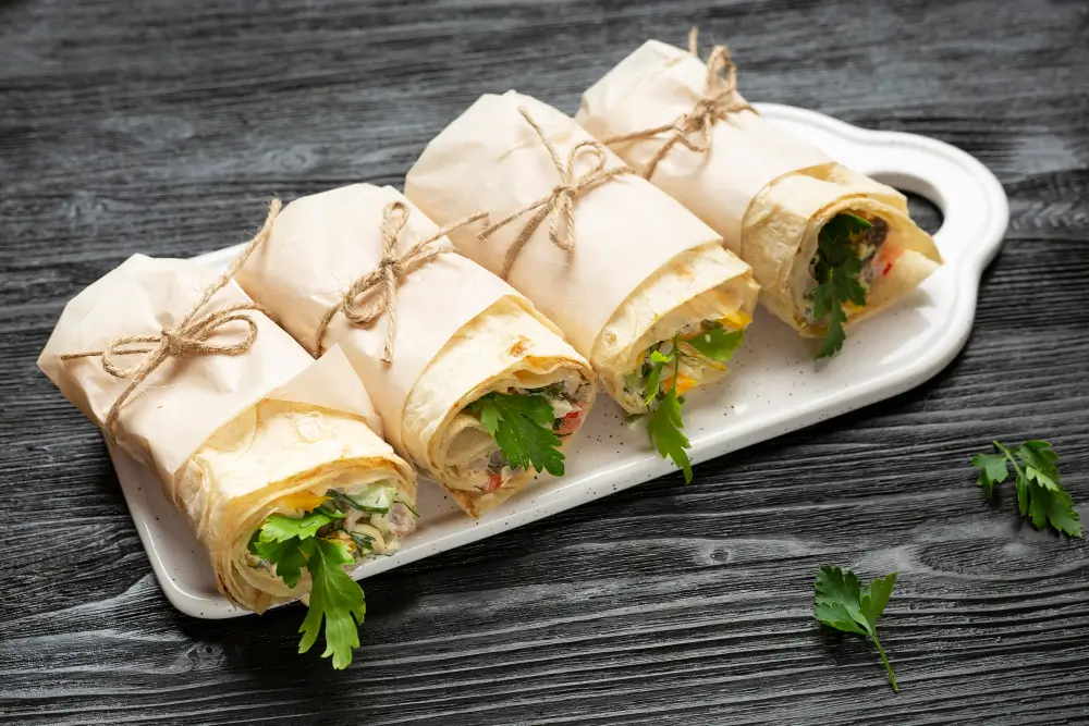 A platter of neatly wrapped shrimp wraps, tied with twine, showcasing a delicious shrimp wrap recipe with fresh ingredients.