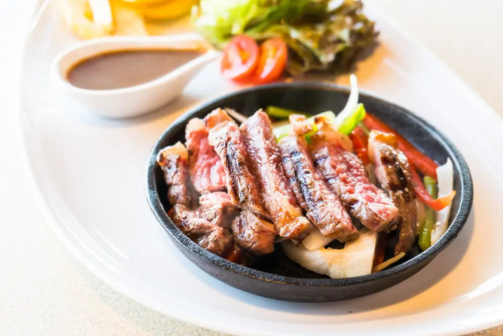 A sizzling plate of beef bacon with grilled vegetables and a side of savory sauce.