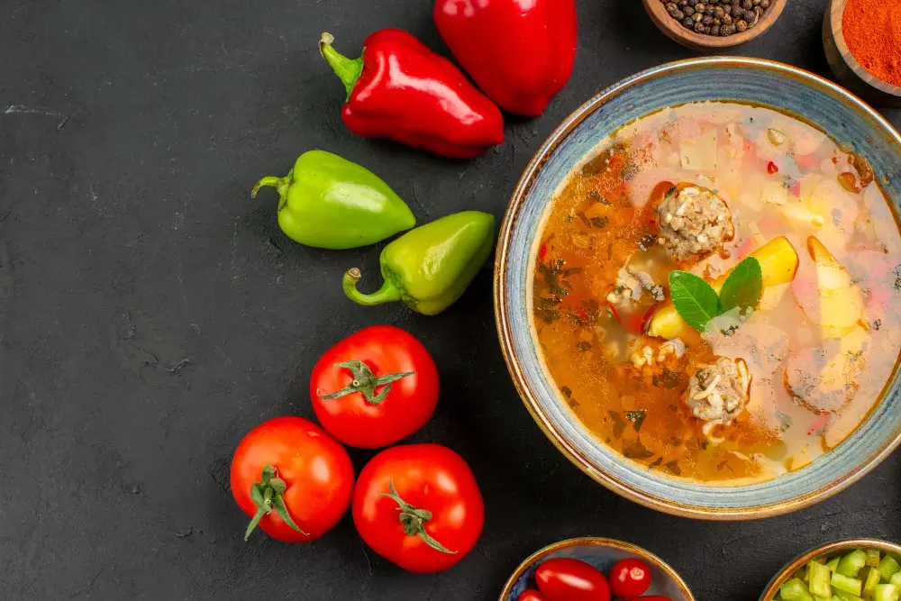 A bowl of hearty Turkey Chili Recipe surrounded by fresh tomatoes, red and green peppers, and spices.