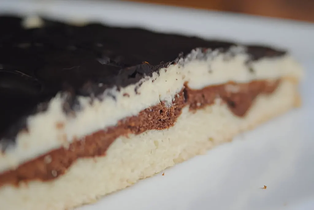 Close-up of a Tandy Cake Recipe slice, revealing layers of creamy filling, rich chocolate, and a soft yellow cake base.