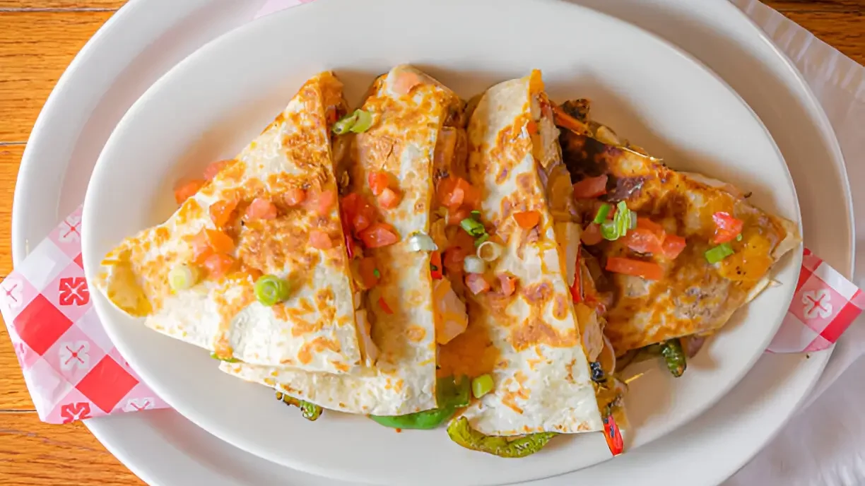 Delicious Chicken Quesadillas served on a white plate, topped with diced tomatoes and green onions.