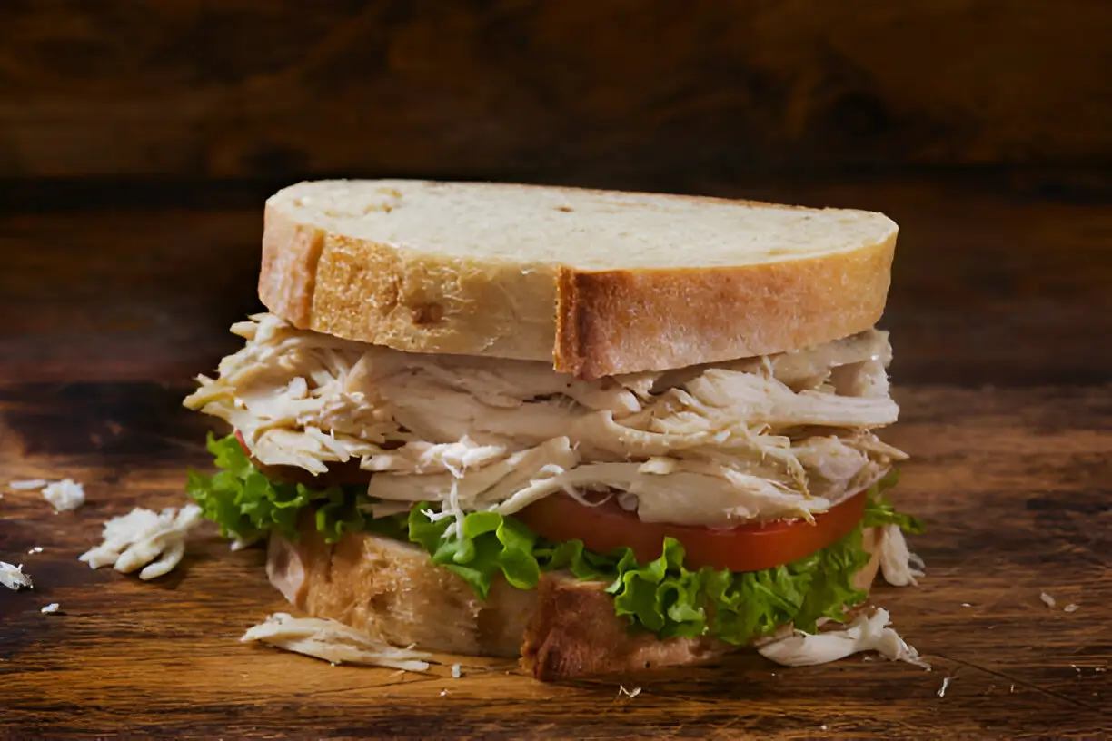 A close-up image of a Chicken Salad Sandwich featuring layers of shredded chicken, lettuce, and tomato between slices of bread.