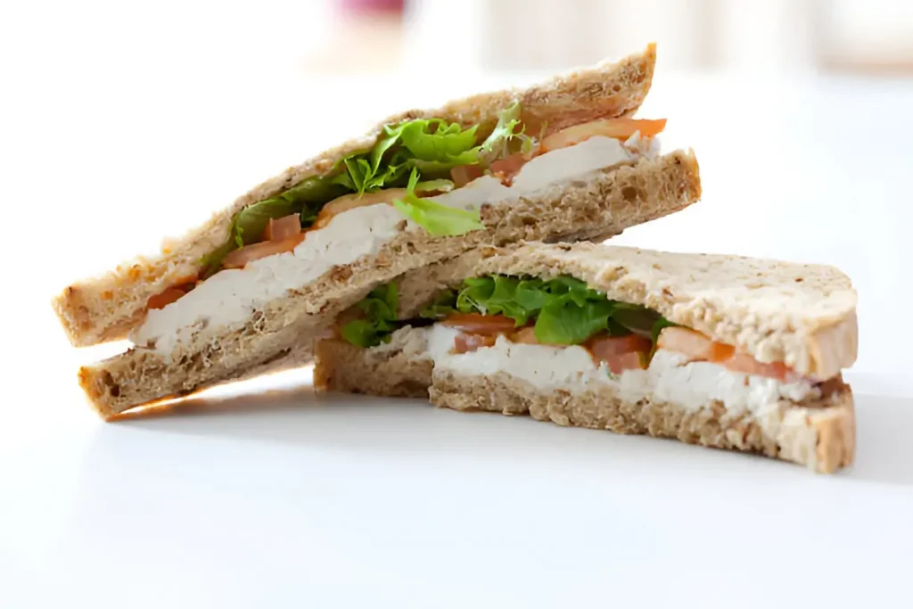 A close-up image of a Chicken Salad Sandwich featuring layers of chicken salad, lettuce, and tomato between slices of whole grain bread.