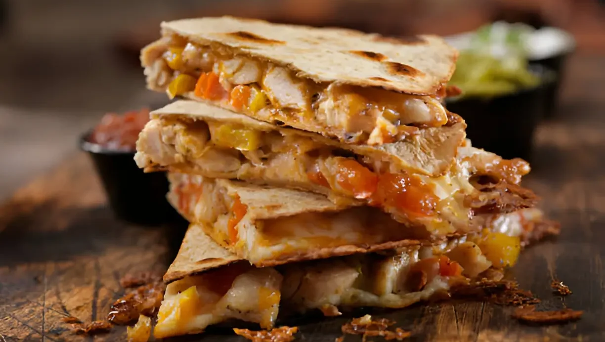 Delicious Chicken Quesadillas stacked on a wooden board, filled with melted cheese, chicken, and colorful vegetables.